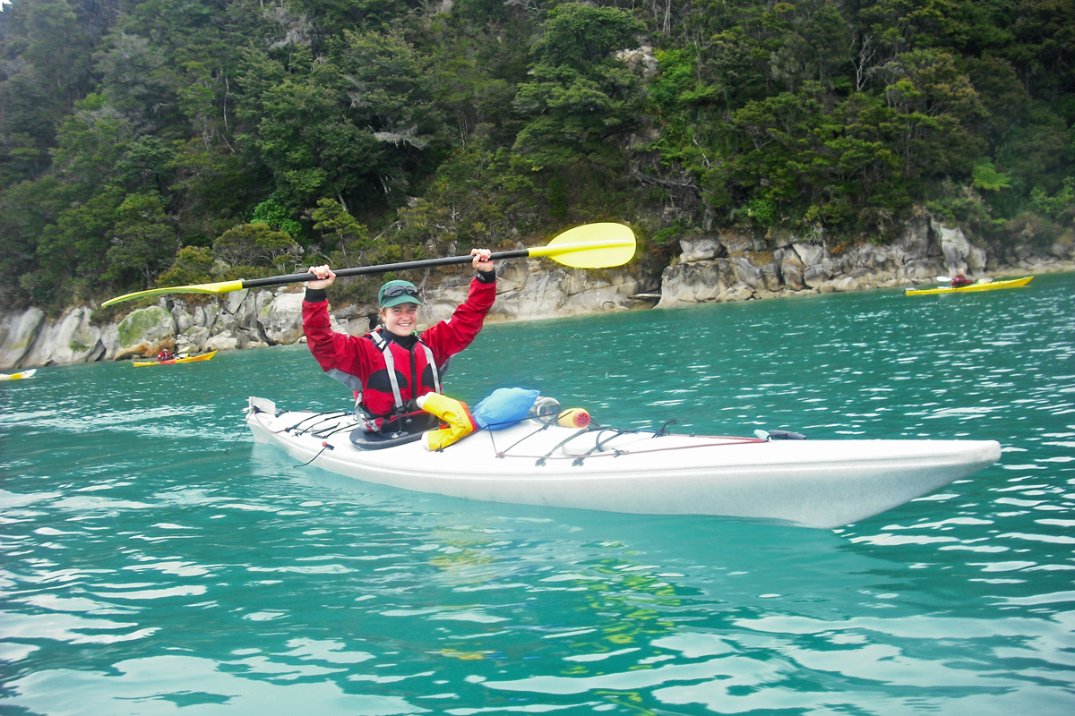 Sea Kayak guide leading a trip with tree lined shore in background. 